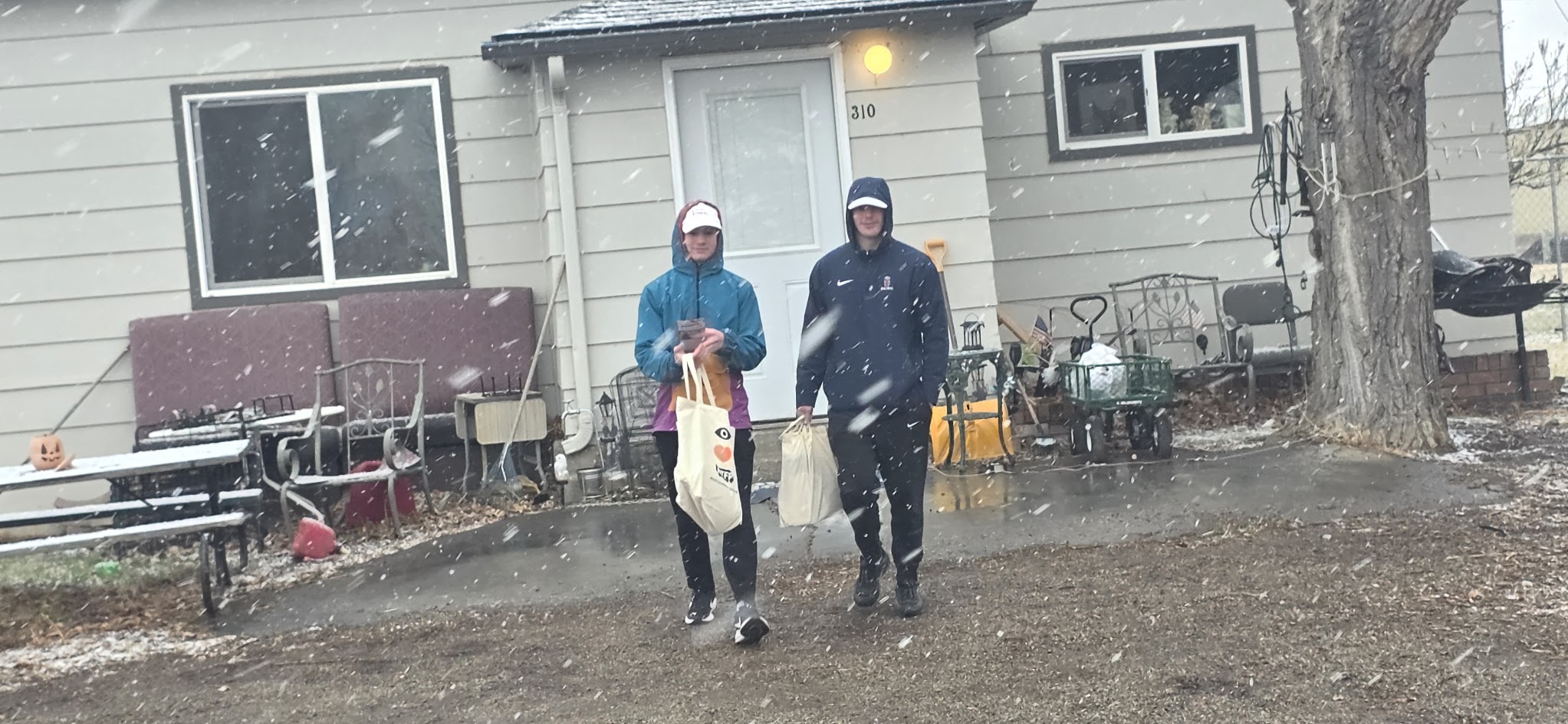 Two volunteers walking away from a house carrying campaign literature bags during a spring snowstorm.